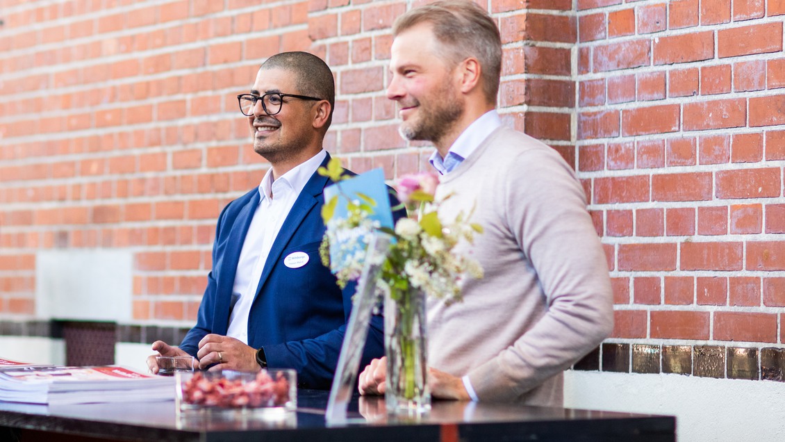 Två kollegor står vid ett bort och ser glada ut på Wihlborgs årstämma 2025