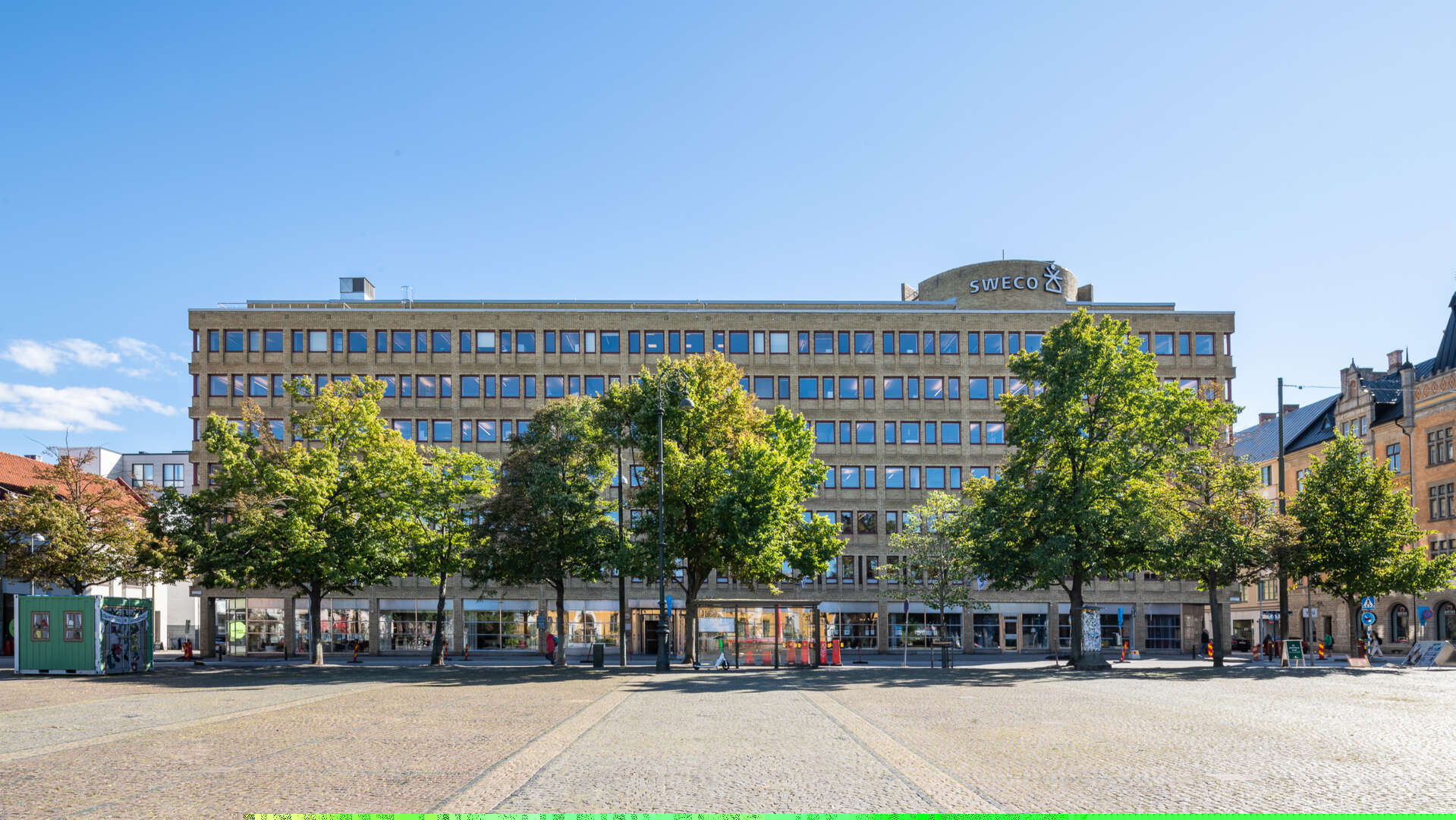 Gul tegelfastighet med Drottningtorget i Malmö i förgrunden.